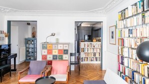 Un salón con piano, estantería, una butaca, sofá y suelo de espiga.