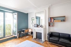 Ein Zimmer mit Schreibtisch, Stuhl, Kamin, Bücherregal und einer schwarzen Ledersofa.