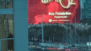 Eine große Werbung für 'The Wizard of Oz' mit rotem Hintergrund und goldener Schrift.