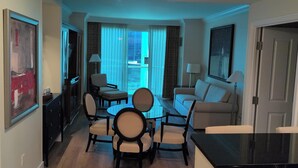 Ein modernes Hotelzimmer mit Essbereich, einer Couch, einem Fernseher und einem großen Fenster mit Vorhängen.