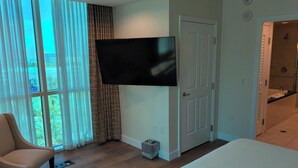 Ein Schlafzimmer mit einem Bett, einem Sessel, einem an der Wand befestigten Fernseher und einer Tür zu einem Badezimmer.