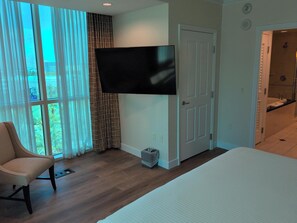 Ein Schlafzimmer mit einem Bett, einem Sessel, einem an der Wand befestigten Fernseher und einer T ür zu einem Badezimmer.