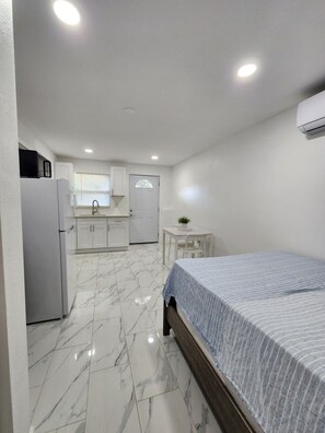 Ein kleines Zimmer mit einem Bett, einem Tisch, einem Waschbecken und einem Kühlschrank.