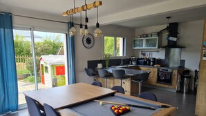 Een moderne keuken met een centraal eiland, een eethoek met een pooltafel, en uitzicht op de tuin.