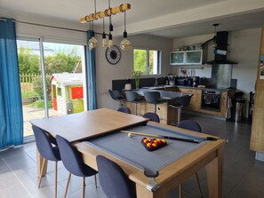 Eine moderne Küche mit einer zentralen Kochinsel, ein Essbereich mit Billardtisch und Blick auf den Garten.