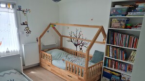 Een kinderkamer met een houten bed, een boekenkast en decoraties aan de muur.