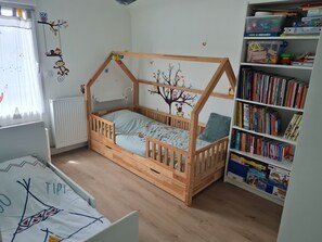 Ein Kinderzimmer mit einem Holzbett, einem Bücherregal und Wanddekorationen.