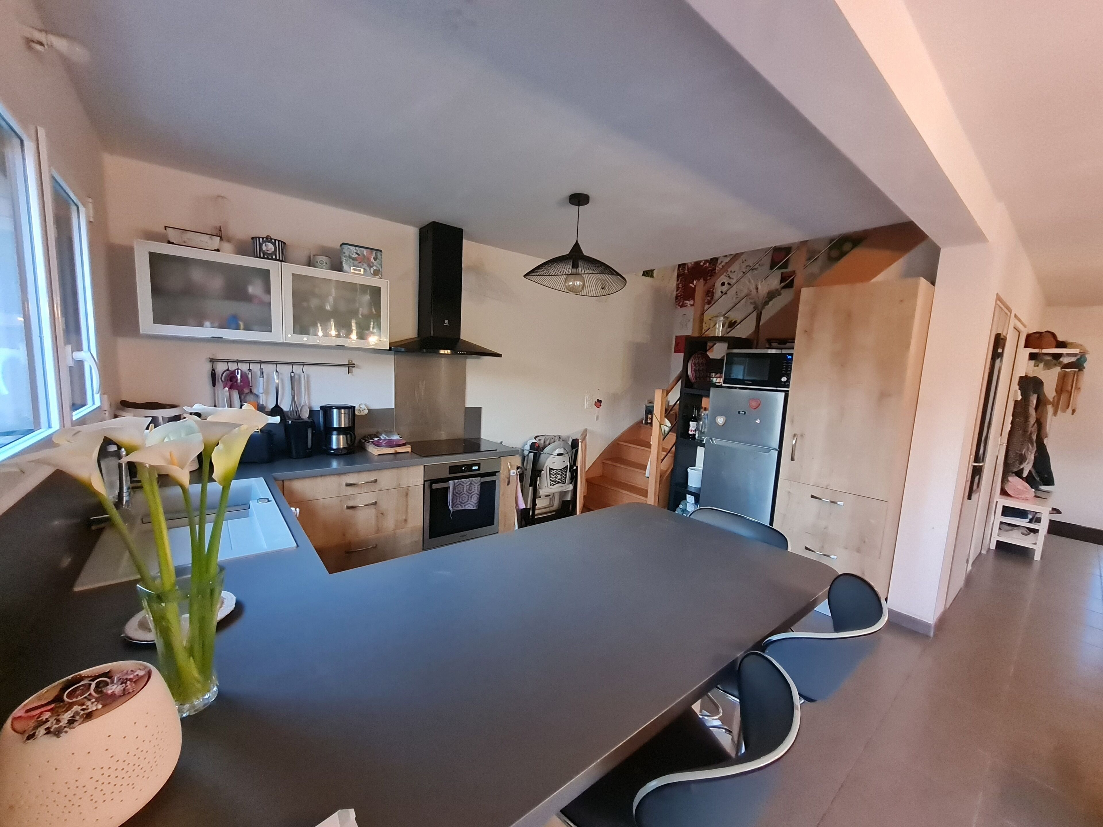 A modern kitchen with a large island, built-in oven, microwave, and a hanging light fixture.