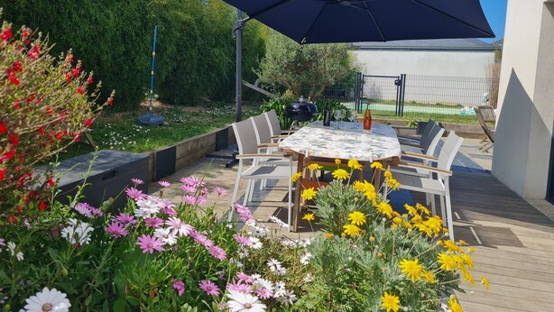 Een terras buiten met een ronde tafel, stoelen en een grote parasol.