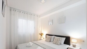 Quarto com cama, cortinas, mesa de cabeceira com abajur e dois objetos decorativos fixados na parede.