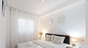 A bedroom with a bed, curtains, a nightstand with a lamp, and two wall-mounted decorative items. - Sol y Brisa Apartment terrace swimming pool and BBQ Orihuela Costa (Orihuela)