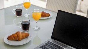 Um laptop sobre uma mesa com dois croissants, dois copos de suco e duas xícaras de café.