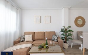 A living room with a brown sofa, a coffee table with a bottle and glasses, a plant, and two framed artworks on the wall. - Sol y Brisa Apartment terrace swimming pool and BBQ Orihuela Costa (Orihuela)