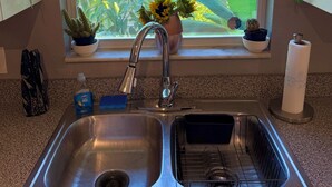 Una cocina con un lavamanos de acero inoxidable, una ventana que ofrece vistas a zonas verdes y una planta en maceta en el alféizar.