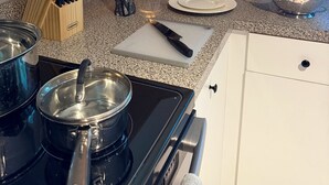 Una cocina con estufa, ollas, cafetera y bloque de cuchillos.