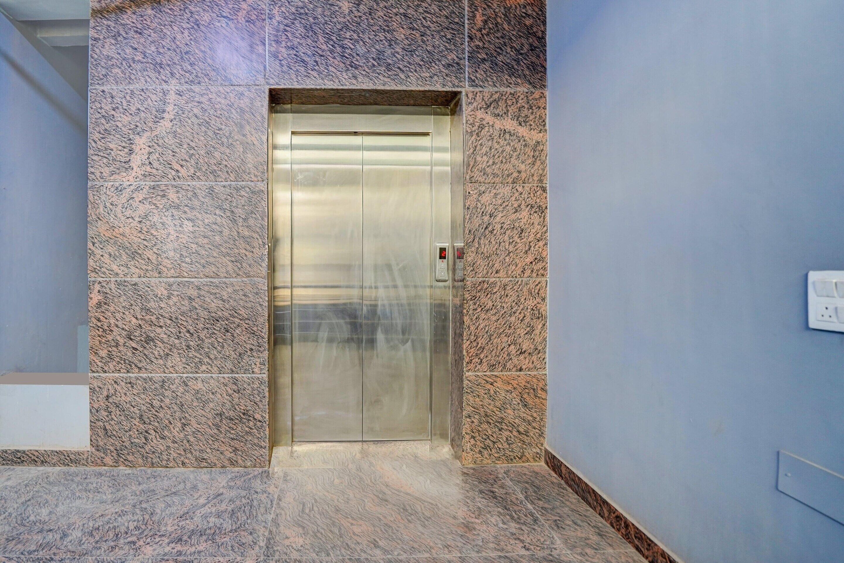 Een moderne lift met een metalen afwerking, geplaatst in een gang met behang van stenen patronen en een blauw geschilderde muur.