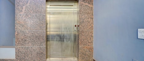 A modern elevator with a metallic finish, set in a hallway with patterned stone walls and a blue painted wall.