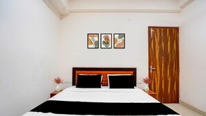 A bedroom with a wooden headboard, a bed with white bedding, two nightstands with vases, and a wooden door. - Classic The Urban (Noida)