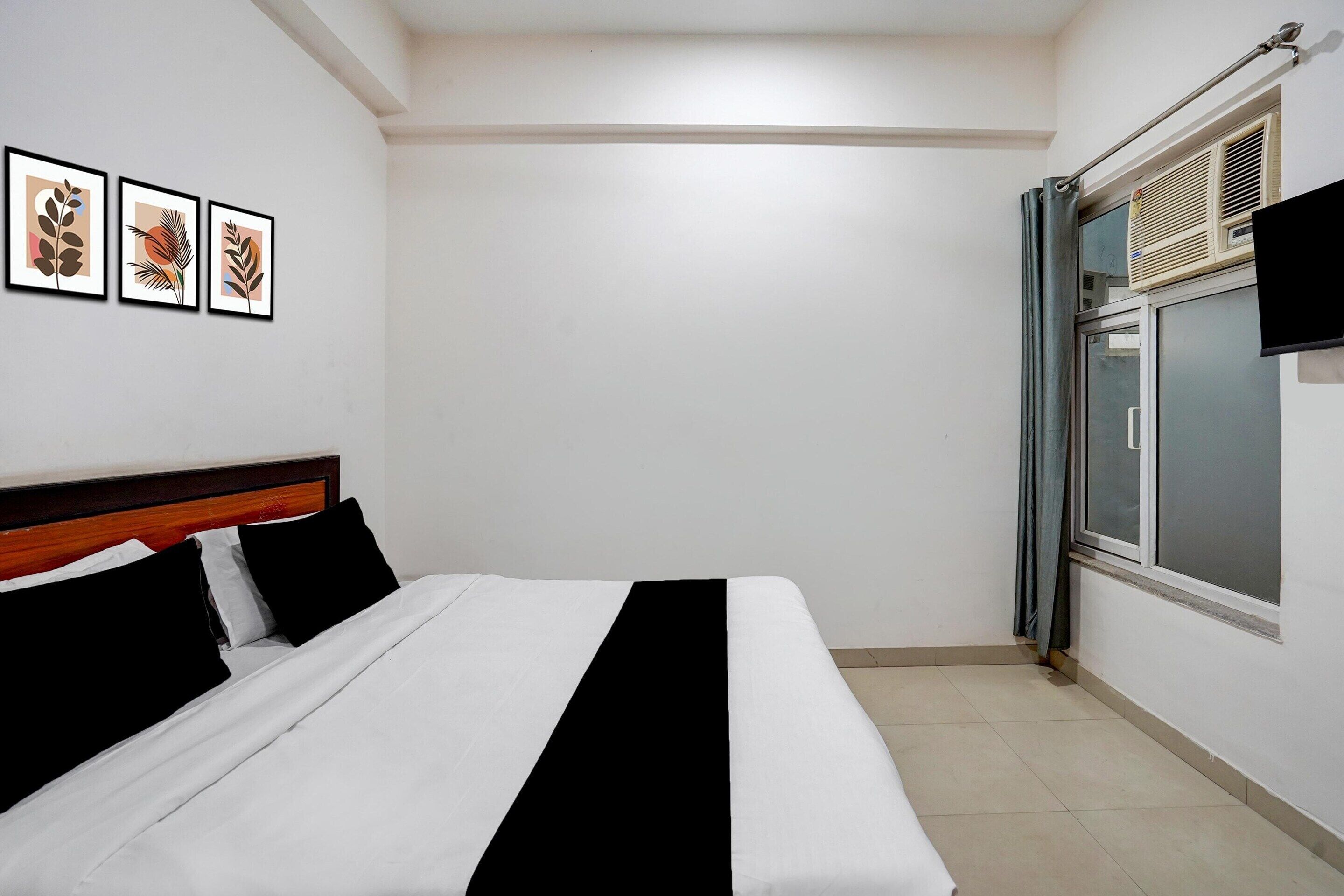 A hotel room with a bed, a window with blinds, and three framed pictures on the wall.