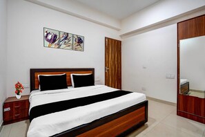 A hotel room with a bed, a nightstand, a mirror, and a wooden wardrobe. - Classic The Urban (Noida)
