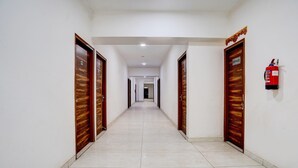 A long, straight hallway with wooden doors on both sides, a fire extinguisher on the right wall, and a ceiling light. - Classic The Urban (Noida)