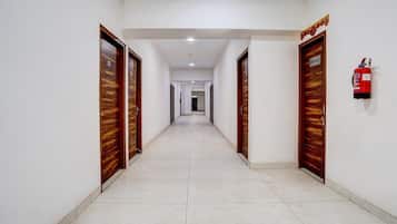 A long, straight hallway with wooden doors on both sides, a fire extinguisher on the right wall, and a ceiling light.
