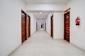 A long, straight hallway with wooden doors on both sides, a fire extinguisher on the right wall, and a ceiling light.