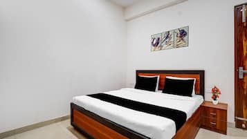 A bedroom with a wooden bed, white bedding, a nightstand with a vase, and a door with a wooden frame.