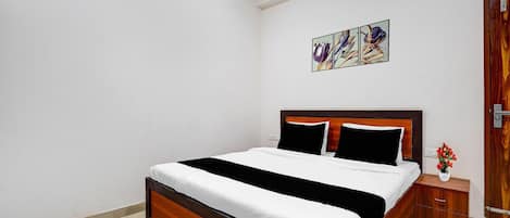 Une chambre à coucher avec un lit en bois, du linge de lit blanc, une table de chevet ornée d’un vase et une porte avec un cadre en bois.