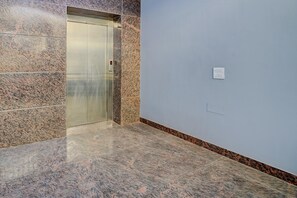 Ein moderner Aufzug mit Metalloptik, einer Wand aus Marmorplatten und einem schlichten, hellen Boden.