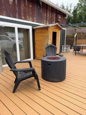 Eine Terrasse mit Feuerstelle, Stühlen und einem Holzhaus mit Schiebetür.
