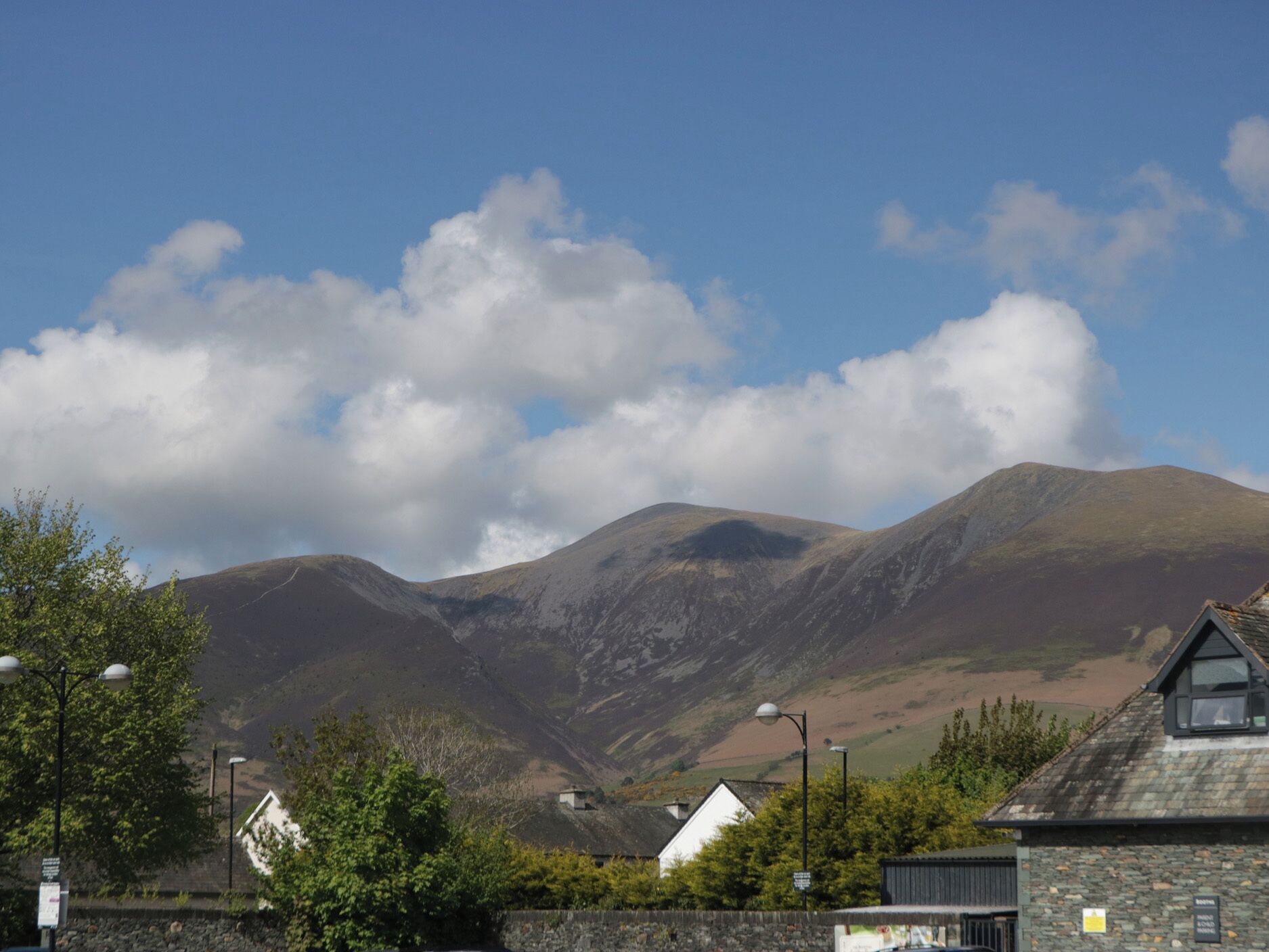 A mountain landscape with a clear sky, a stone building with a sloped roof, and a white house with a chimney.