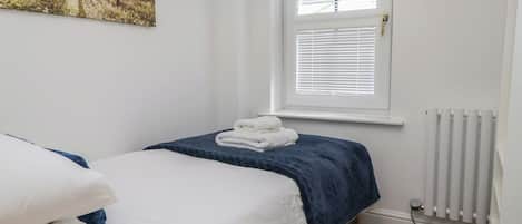 A bedroom with a bed, a window with blinds, a radiator, and a painting on the wall.
