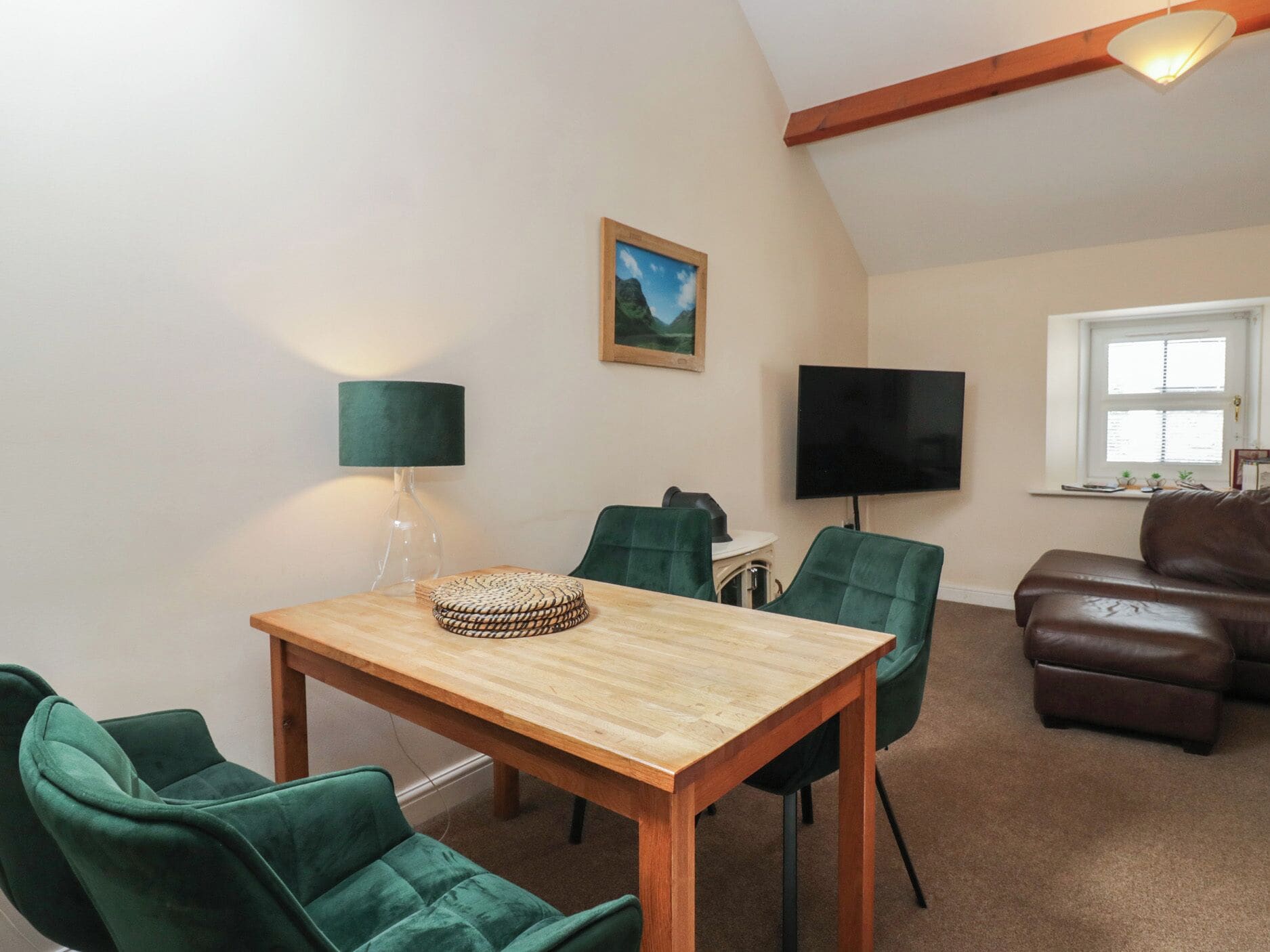 A living room with a wooden table, green chairs, a leather sofa, a TV, and a framed picture on the wall.