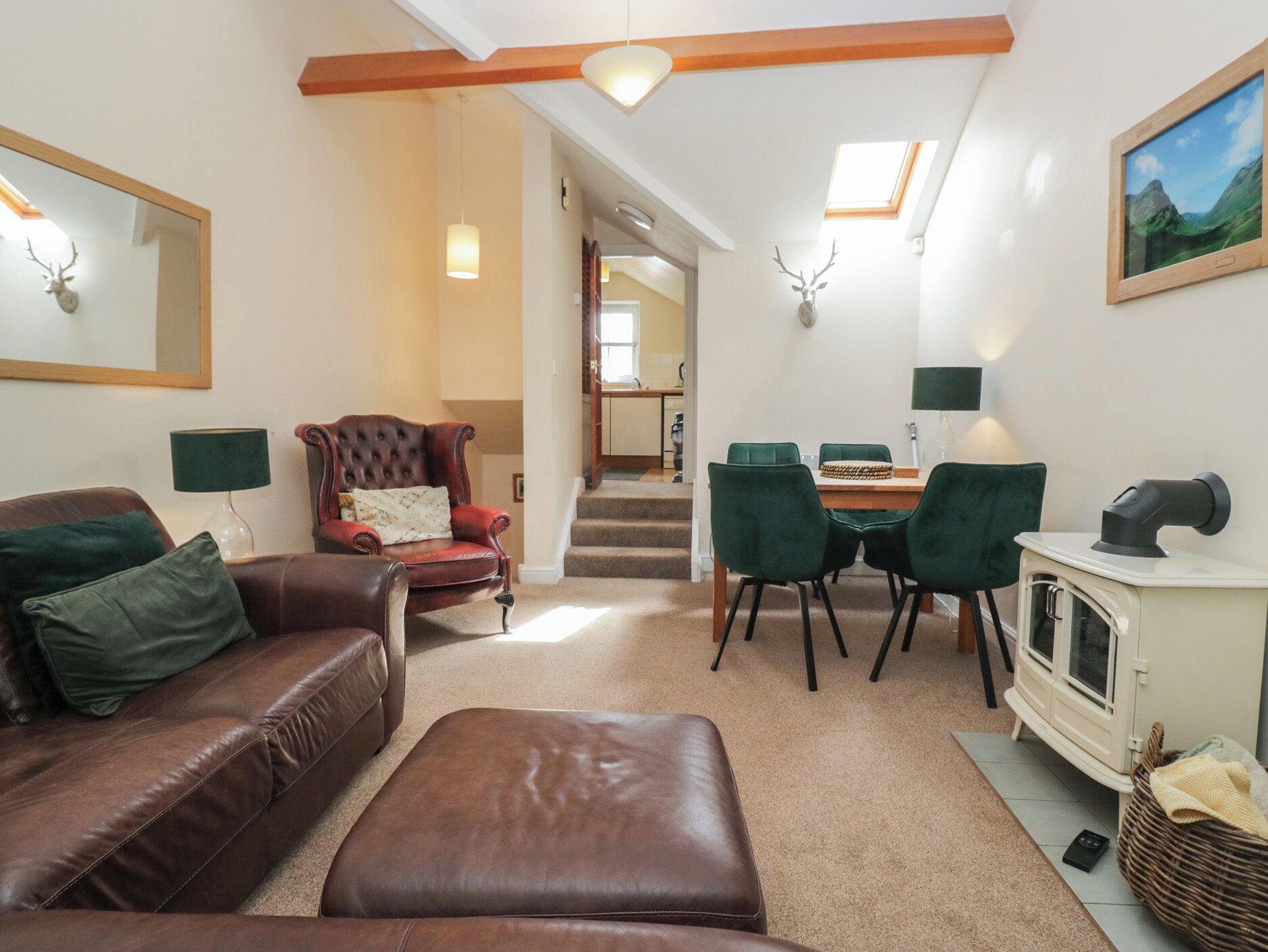 A living room with a brown leather sofa, a tufted armchair, a dining area with a table and chairs, a fireplace, and a staircase leading to an upper level.