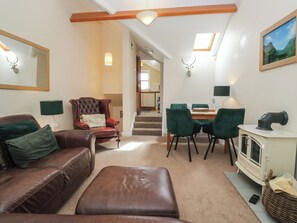 Ein Wohnzimmer mit braunem Ledersofa, einem gepolsterten Sessel, einem Essbereich mit Tisch und Stühlen, einem Kamin und einer Treppe, die zu einer oberen Ebene führt.