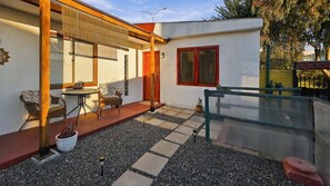 A patio with a table and chairs, a small garden area with gravel, and a building with a red door and windows.