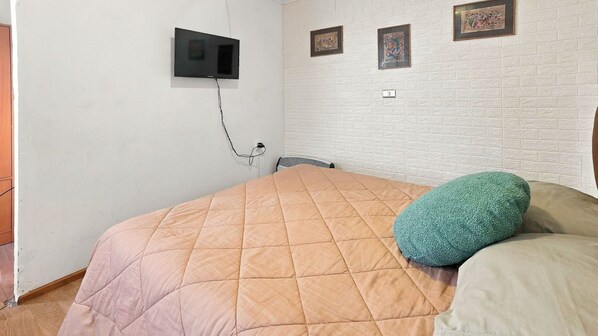 A bedroom with a bed, a wall-mounted TV, and three framed artworks.