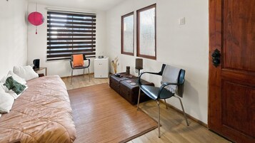Een slaapkamer met een bed, een stoel, een klein tafeltje, een koffer en een deur.