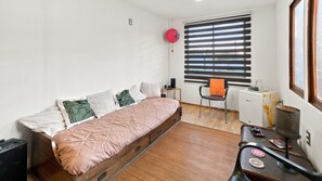 A compact room with a bed, a chair, a small table, and a radiator.