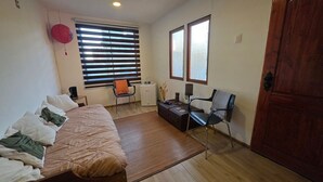 A bedroom with a bed, two chairs, a small table, a heater, and a window. - Oceana Suites Bosques de Montemar (Concón)