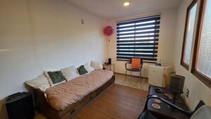 A small, neatly arranged bedroom with a bed, a chair, a desk, and a radiator. - Oceana Suites Bosques de Montemar (Concón)
