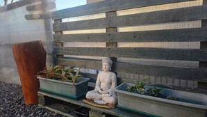 A statue of a seated figure on a wooden bench, surrounded by potted plants. - Oceana Suites Bosques de Montemar (Concón)