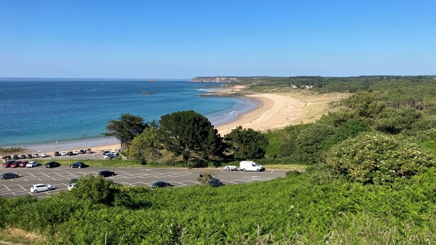 Vista costera con aparcamiento, playa y vegetación.