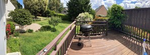 A wooden deck with a barbecue grill, surrounded by a fenced garden with various plants and trees. - 3-bedroom house with garden 1 km from Anse du Croc beach (Fréhel)