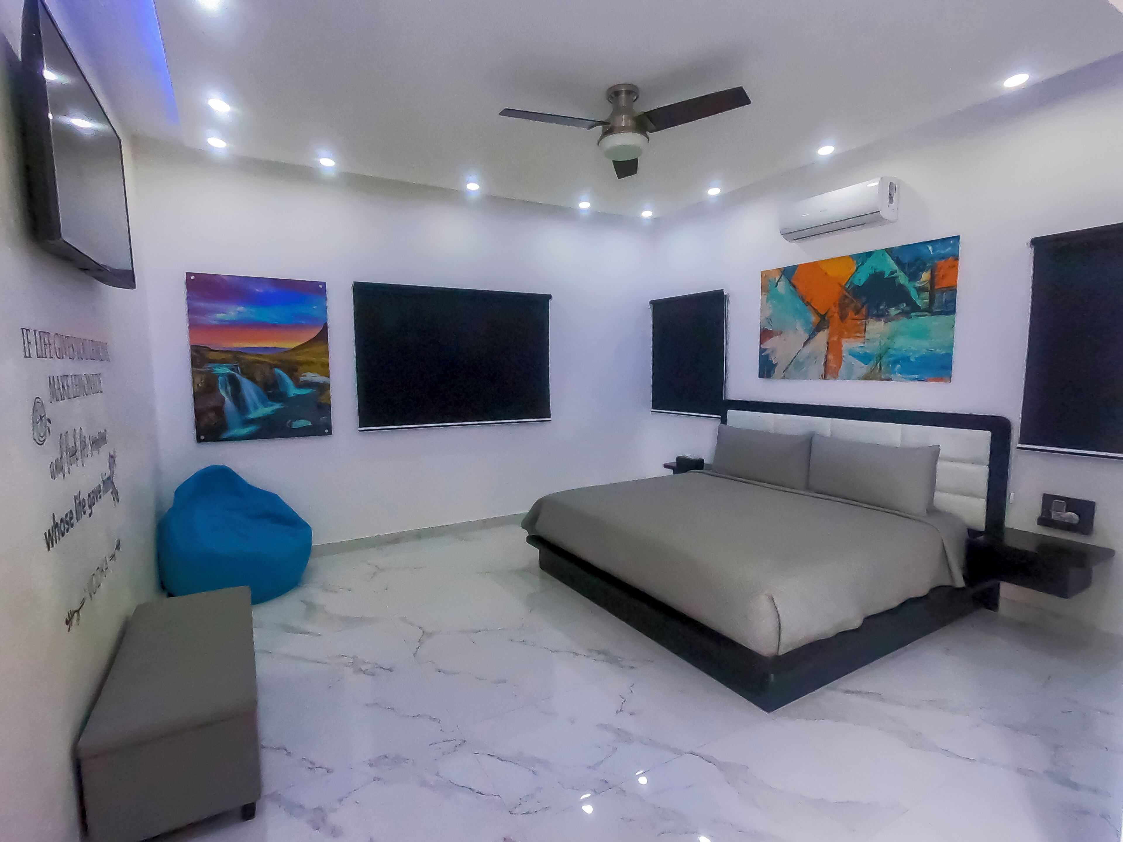 A bedroom with a bed, a ceiling fan, recessed lighting, a wall-mounted air conditioner, and artwork.