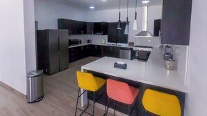 Una cucina moderna con mobili scuri, un piano di lavoro bianco, un fornello e due sgabelli da bar.