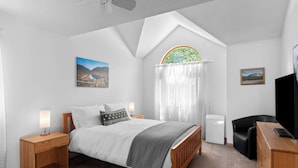 Una camera da letto con un letto, comodini, una scrivania, una sedia, una televisione e una finestra con tende.