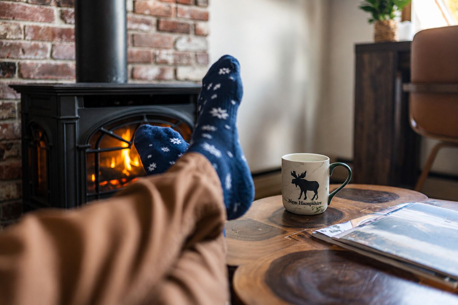 A cozy room with a fireplace, a mug with a moose design, and a person relaxing with a book.