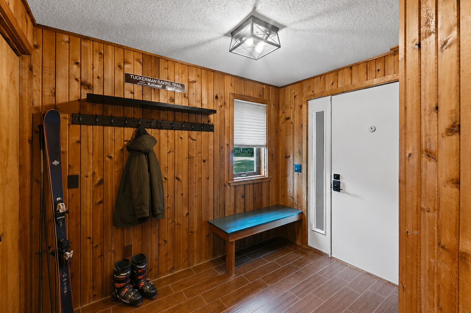 Un interior de madera con un banco, un perchero, esquíes y una puerta.